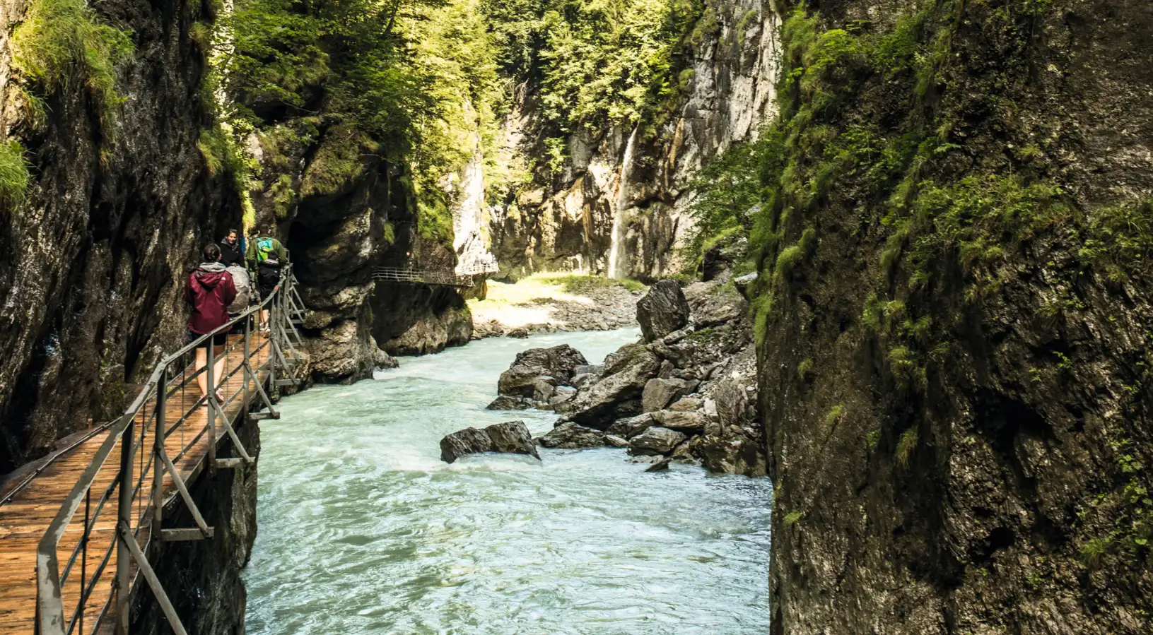 Hikers walking along the wooden boardwalk bolted to the cliffside inside the narrow Aare Gorge, one of the unique natural things to do in Interlaken nearby.