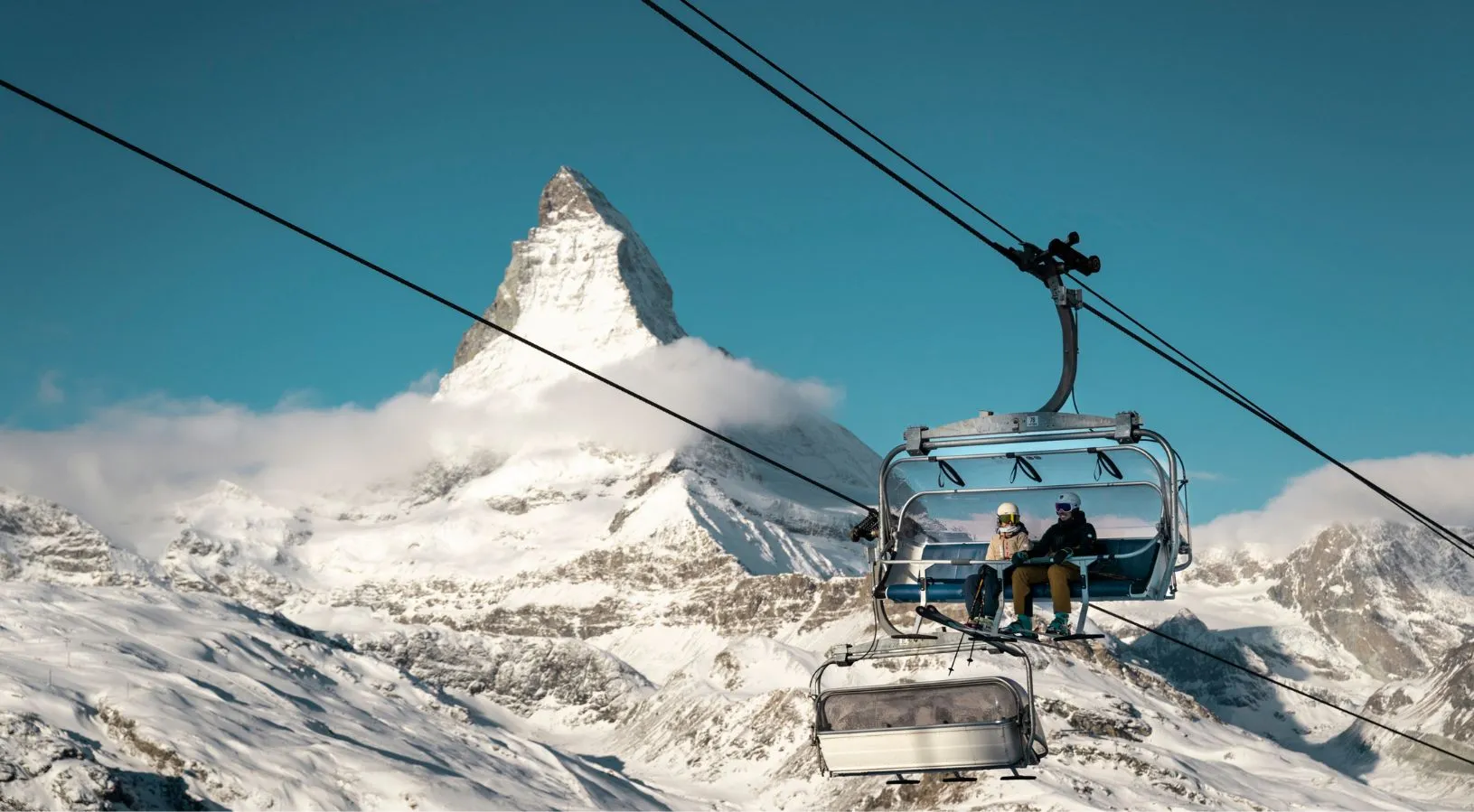 Couple riding a ski lift with the iconic Matterhorn in the background, a signature winter experience featured in Switzerland honeymoon packages.