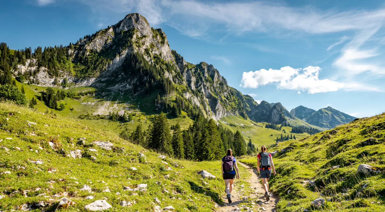 A bright summer day in Switzerland with turquoise lake water, green alpine meadows, and hikers exploring mountain trails, suggesting that the best time to visit Switzerland is during warm sunny months.