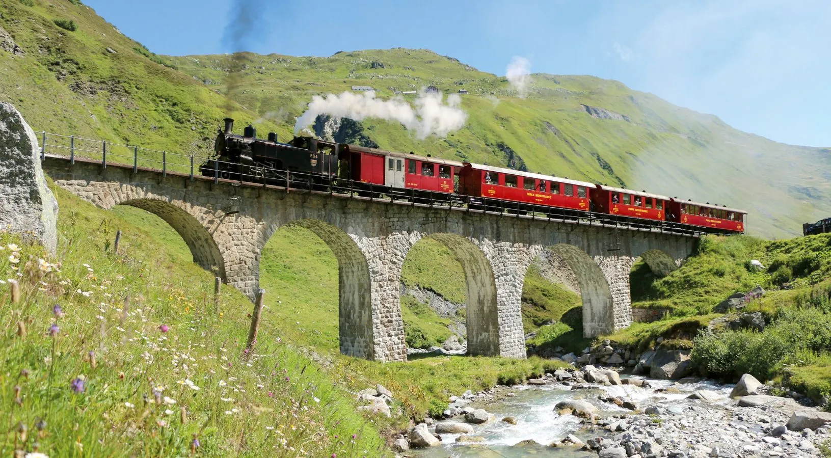 Steam train crossing a stone viaduct in the Swiss Alps, showcasing scenic rail journeys explained in How the Swiss Travel Pass Works on Trains.