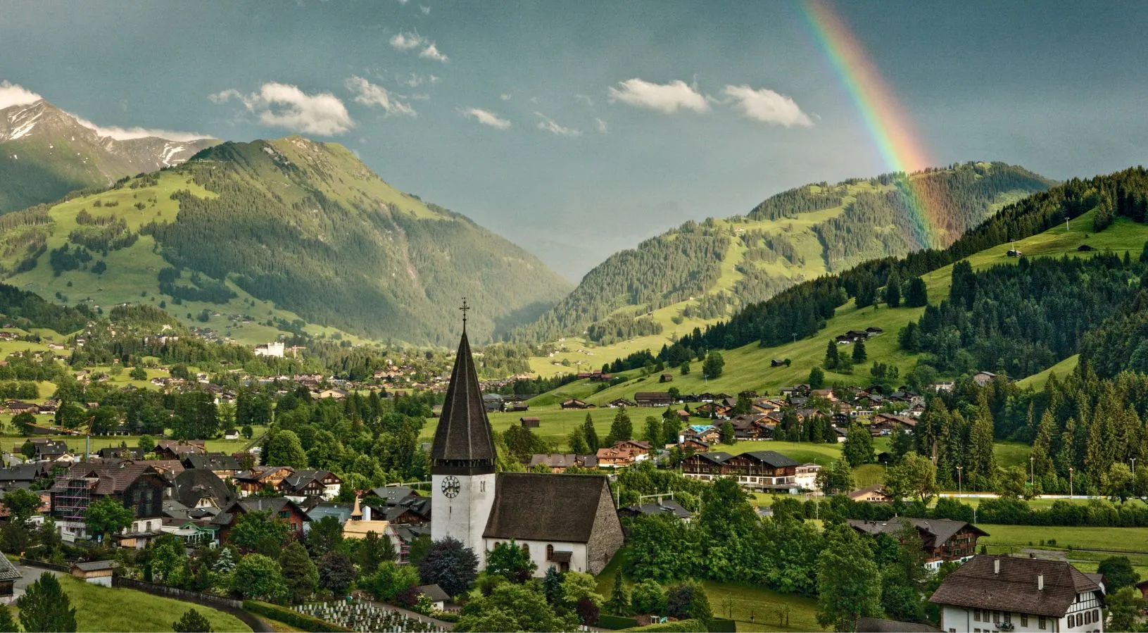 Traditional Swiss village with alpine landscape and rainbow, accessible using Swiss Travel Pass for 3, 4 or 8 days
