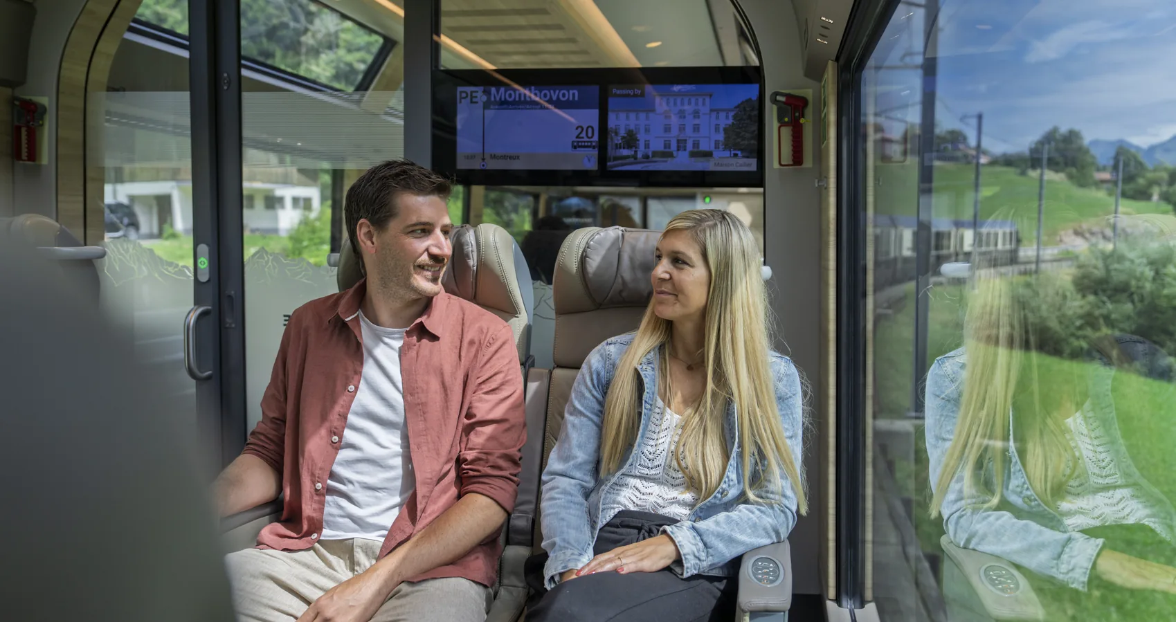 Couple sitting side by side in the panoramic carriage of the GoldenPass Prestige train near Montbovon