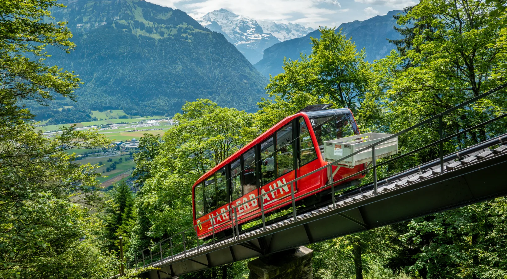 The red Harderbahn funicular climbing the steep forested mountainside from Interlaken up to Harder Kulm in the Bernese Oberland, Switzerland