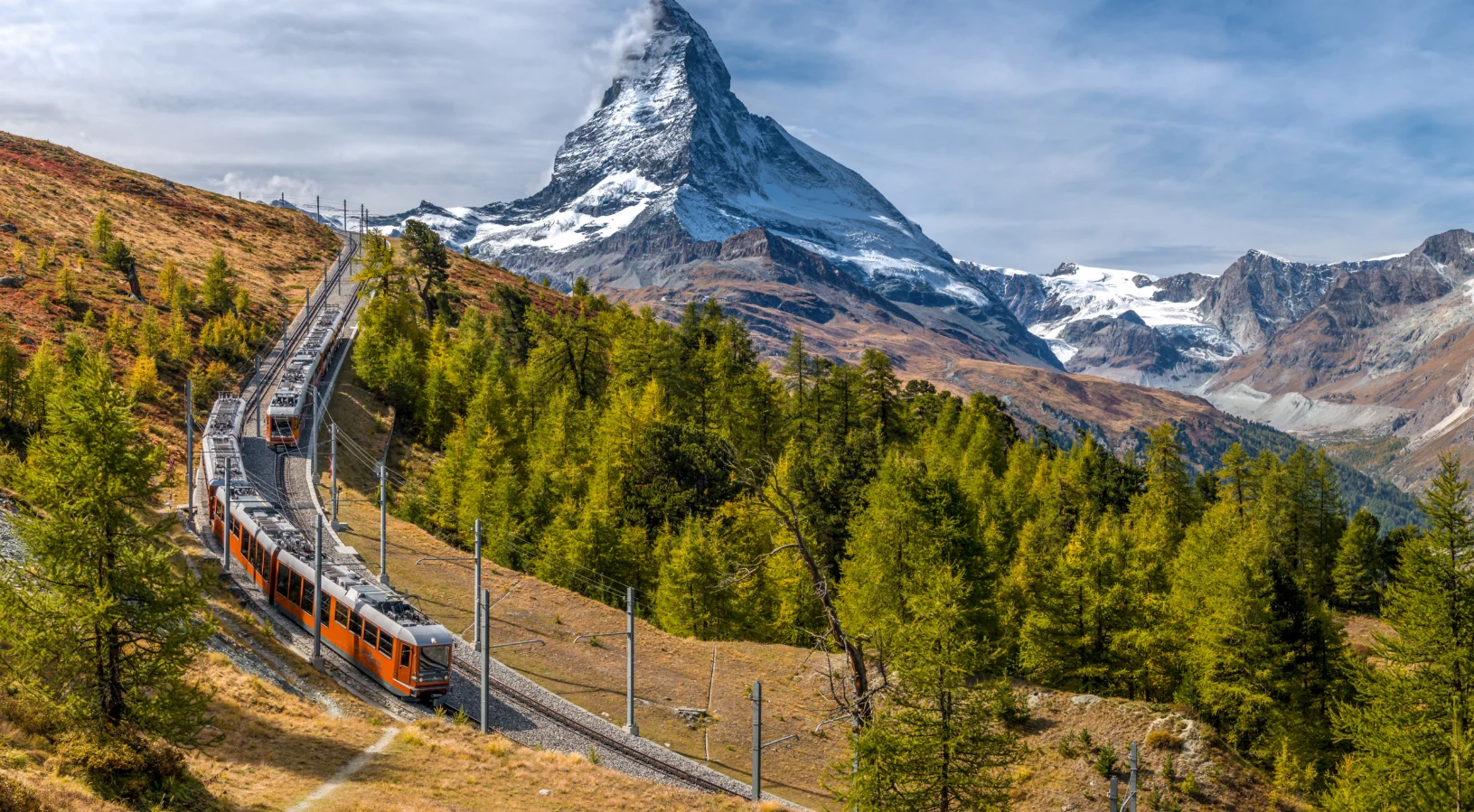 The Gornergrat Railway climbing through larch forest above Zermatt with the Matterhorn behind, illustrating whether the Swiss Travel Pass is worth it on a multi-city trip