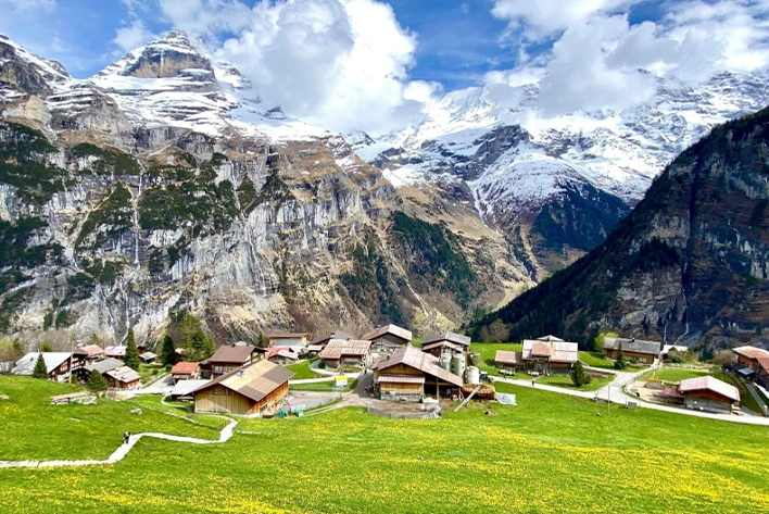 Scenic view of Mürren in Lauterbrunnen, Switzerland, featuring charming alpine chalets, lush green meadows, and the stunning backdrop of the Swiss Alps under a clear blue sky.