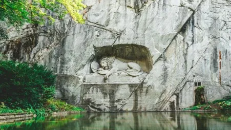 A close-up view of the Reclining Lion Statue in Lucerne, a poignant monument carved into a sandstone rock, depicting a dying lion as a tribute to Swiss Guards who died during the French Revolution, surrounded by lush greenery and a tranquil atmosphere.