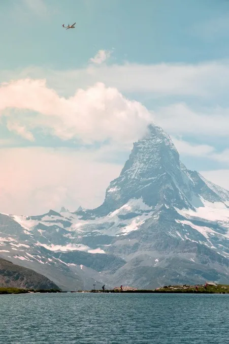 A stunning view of the Zermatt landscape, featuring the iconic Matterhorn mountain towering above lush valleys, with serene lakes reflecting the peaks, framed by green meadows and clear blue skies.